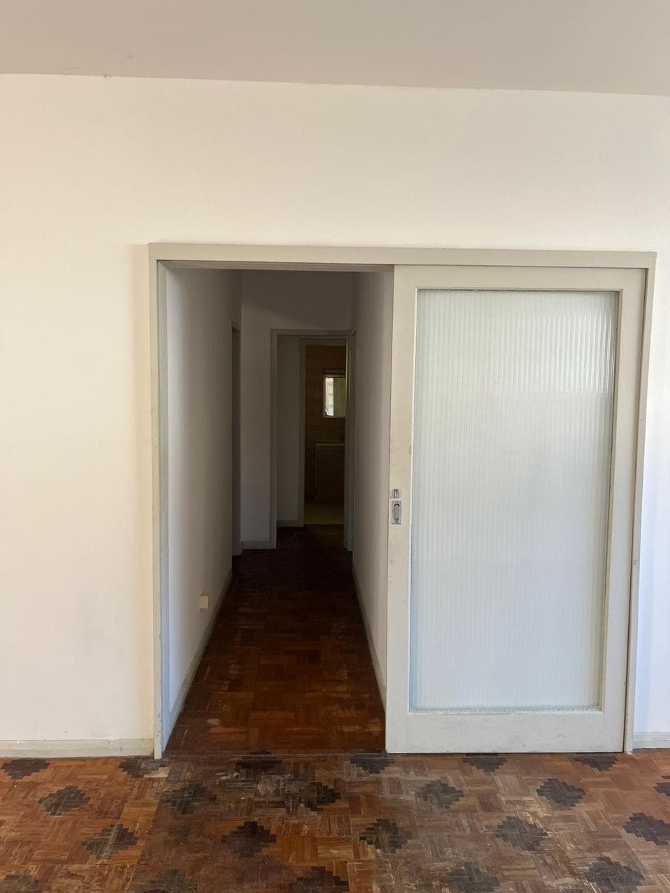 Corredor com porta de vidro jateado e piso de taco, antes da reforma